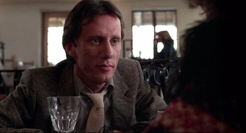 Movie still from “Videodrome” (1983), directed by David Cronenberg – A man sitting at a table with a glass of wine in front of him; Close Up shot, Low angle