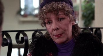 Movie still from “Videodrome” (1983), directed by David Cronenberg – An older woman wearing a purple sweater and a purple hat; Close Up shot, Over the shoulder angle