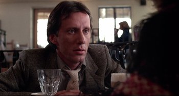 Movie still from “Videodrome” (1983), directed by David Cronenberg – A man sitting at a table with a glass of wine; Close Up shot, Low angle