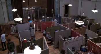 Movie still from “Videodrome” (1983), directed by David Cronenberg – A group of people sitting in a room with cubicle walls; Extreme Wide shot, High angle