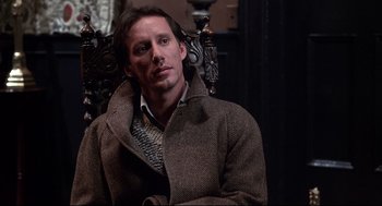 Movie still from “Videodrome” (1983), directed by David Cronenberg – A man in a brown coat sitting on a chair; Close Up shot, Low angle