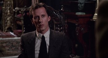 Movie still from “Videodrome” (1983), directed by David Cronenberg – A man wearing a suit and tie sitting in a chair; Close Up shot, Low angle