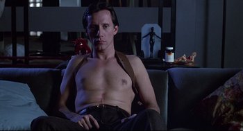 Movie still from “Videodrome” (1983), directed by David Cronenberg – A man sitting on a couch in a living room; Medium shot, Low angle