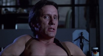 Movie still from “Videodrome” (1983), directed by David Cronenberg – A man with no shirt is sitting in a chair; Close Up shot, Low angle