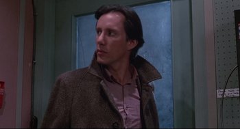 Movie still from “Videodrome” (1983), directed by David Cronenberg – A man wearing a brown coat standing in front of a wall; Close Up shot, Low angle