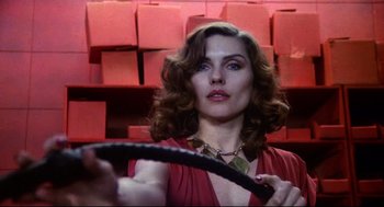 Movie still from “Videodrome” (1983), directed by David Cronenberg – A woman in a red dress holding a whip in front of a wall; Close Up shot, Low angle