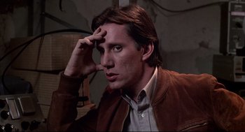 Movie still from “Videodrome” (1983), directed by David Cronenberg – A young man is looking at the camera while holding his hand up to his forehead; Close Up shot, Low angle
