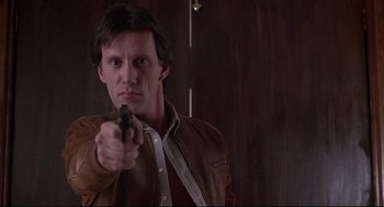 Movie still from “Videodrome” (1983), directed by David Cronenberg – A man holding a gun in a room; Close Up shot, Low angle