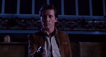 Movie still from “Videodrome” (1983), directed by David Cronenberg – A man in a brown leather jacket holding a gun; Close Up shot, Low angle
