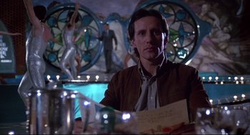 Movie still from “Videodrome” (1983), directed by David Cronenberg – A man sitting at a table in front of a mirror; Medium shot, Low angle