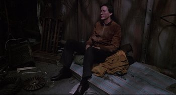 Movie still from “Videodrome” (1983), directed by David Cronenberg – A man sitting on the ground in a room; Medium shot, High angle
