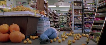 Movie still from “Village of the Damned” (1995), directed by John Carpenter – A person laying on the ground in a grocery store; Wide shot, Overhead angle