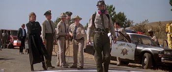 Movie still from “Village of the Damned” (1995), directed by John Carpenter – A group of men standing next to each other on the side of the road; Wide shot, Low angle