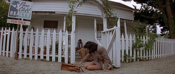 Movie still from “Village of the Damned” (1995), directed by John Carpenter – A woman kneeling on the ground outside of a house; Wide shot, Low angle