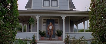 Movie still from “Village of the Damned” (1995), directed by John Carpenter – A woman standing in front of a house with plants; Wide shot, Low angle
