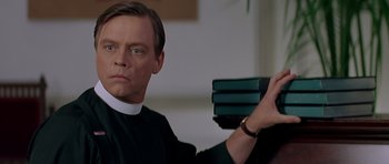 Movie still from “Village of the Damned” (1995), directed by John Carpenter – A man holding a stack of books in his hands; Close Up shot, Low angle