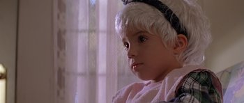 Movie still from “Village of the Damned” (1995), directed by John Carpenter – A little girl wearing a pink robe and a white hat; Close Up shot, High angle