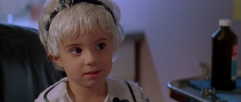 Movie still from “Village of the Damned” (1995), directed by John Carpenter – A little girl with blonde hair wearing a headband; Close Up shot, High angle