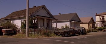 Movie still from “Village of the Damned” (1995), directed by John Carpenter – An old car is parked in front of a house; Wide shot, Low angle