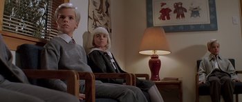 Movie still from “Village of the Damned” (1995), directed by John Carpenter – Two people sitting in a living room next to a lamp; Medium shot, Low angle