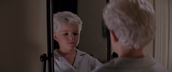Movie still from “Village of the Damned” (1995), directed by John Carpenter – A young boy looking at his reflection in a mirror; Close Up shot, Low angle