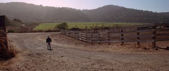 Movie still from “Village of the Damned” (1995), directed by John Carpenter – A man standing in a dirt field next to a fence; Extreme Wide shot, High angle