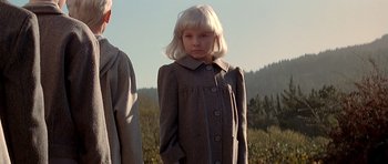 Movie still from “Village of the Damned” (1995), directed by John Carpenter – A young girl with blonde hair wearing a gray coat; Medium shot, Low angle