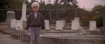 Movie still from “Village of the Damned” (1995), directed by John Carpenter – A young boy standing next to a stone wall; Wide shot, Low angle