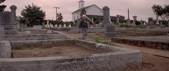 Movie still from “Village of the Damned” (1995), directed by John Carpenter – An older woman is walking through a cemetery; Wide shot, Low angle