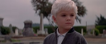 Movie still from “Village of the Damned” (1995), directed by John Carpenter – A young boy with white hair is looking at the camera; Close Up shot, High angle