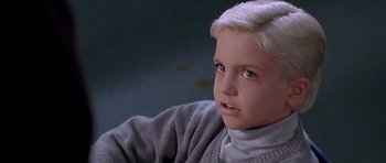 Movie still from “Village of the Damned” (1995), directed by John Carpenter – A young boy with blonde hair wearing a gray sweater; Close Up shot, High angle