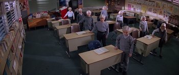 Movie still from “Village of the Damned” (1995), directed by John Carpenter – A group of older people standing in a classroom; Wide shot, High angle