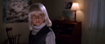 Movie still from “Village of the Damned” (1995), directed by John Carpenter – A girl with white hair is standing in a room; Close Up shot, Low angle