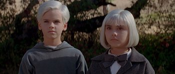 Movie still from “Village of the Damned” (1995), directed by John Carpenter – Two young people standing next to each other in front of a tree; Close Up shot, High angle