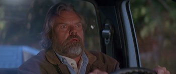 Movie still from “Village of the Damned” (1995), directed by John Carpenter – A man with a beard is driving a car; Close Up shot, Low angle