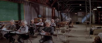 Movie still from “Village of the Damned” (1995), directed by John Carpenter – A group of people sitting at a table in a room; Wide shot, High angle