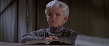 Movie still from “Village of the Damned” (1995), directed by John Carpenter – A young boy sitting in front of an open book; Close Up shot, High angle