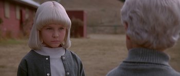 Movie still from “Village of the Damned” (1995), directed by John Carpenter – A young girl and an older man are standing in a field; Close Up shot, Over the shoulder angle