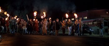 Movie still from “Village of the Damned” (1995), directed by John Carpenter – A group of people holding torches on a street; Wide shot, High angle