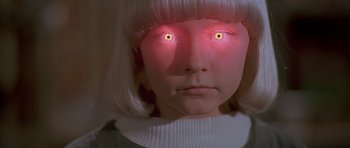 Movie still from “Village of the Damned” (1995), directed by John Carpenter – A girl with glowing red eyes stares into the camera; Close Up shot, High angle