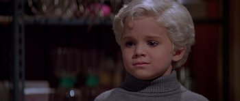 Movie still from “Village of the Damned” (1995), directed by John Carpenter – A young boy with blonde hair wearing a gray sweater; Close Up shot, High angle