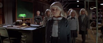 Movie still from “Village of the Damned” (1995), directed by John Carpenter – A group of people standing in a room; Medium shot, High angle