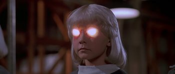 Movie still from “Village of the Damned” (1995), directed by John Carpenter – A woman with glowing eyes is standing in a dimly - lit room; Close Up shot, Low angle