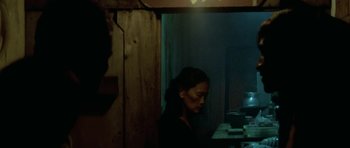 Movie still from “Vinyan” (2008), directed by Fabrice du Welz – A woman sitting at a table in front of a window; Medium shot, Over the shoulder angle