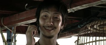 Movie still from “Vinyan” (2008), directed by Fabrice du Welz – A young man smiles while talking on a cell phone; Close Up shot, Low angle