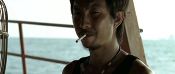 Movie still from “Vinyan” (2008), directed by Fabrice du Welz – A man smoking a cigarette in front of a body of water; Close Up shot, Low angle