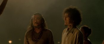 Movie still from “Vinyan” (2008), directed by Fabrice du Welz – Two men standing next to each other in a dark room; Medium shot, Low angle