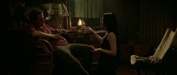 Movie still from “Vinyan” (2008), directed by Fabrice du Welz – A man and a woman sitting in a living room next to a fireplace; Medium shot, High angle
