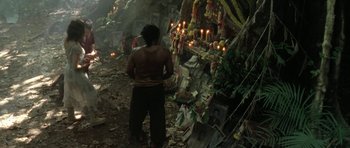 Movie still from “Vinyan” (2008), directed by Fabrice du Welz – A man standing in front of a shrine with candles lit; Wide shot, High angle