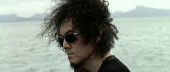 Movie still from “Vinyan” (2008), directed by Fabrice du Welz – A person wearing sunglasses near a body of water; Close Up shot, Low angle
